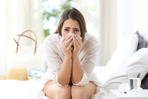 a woman sneezing into a kleenex in her home
